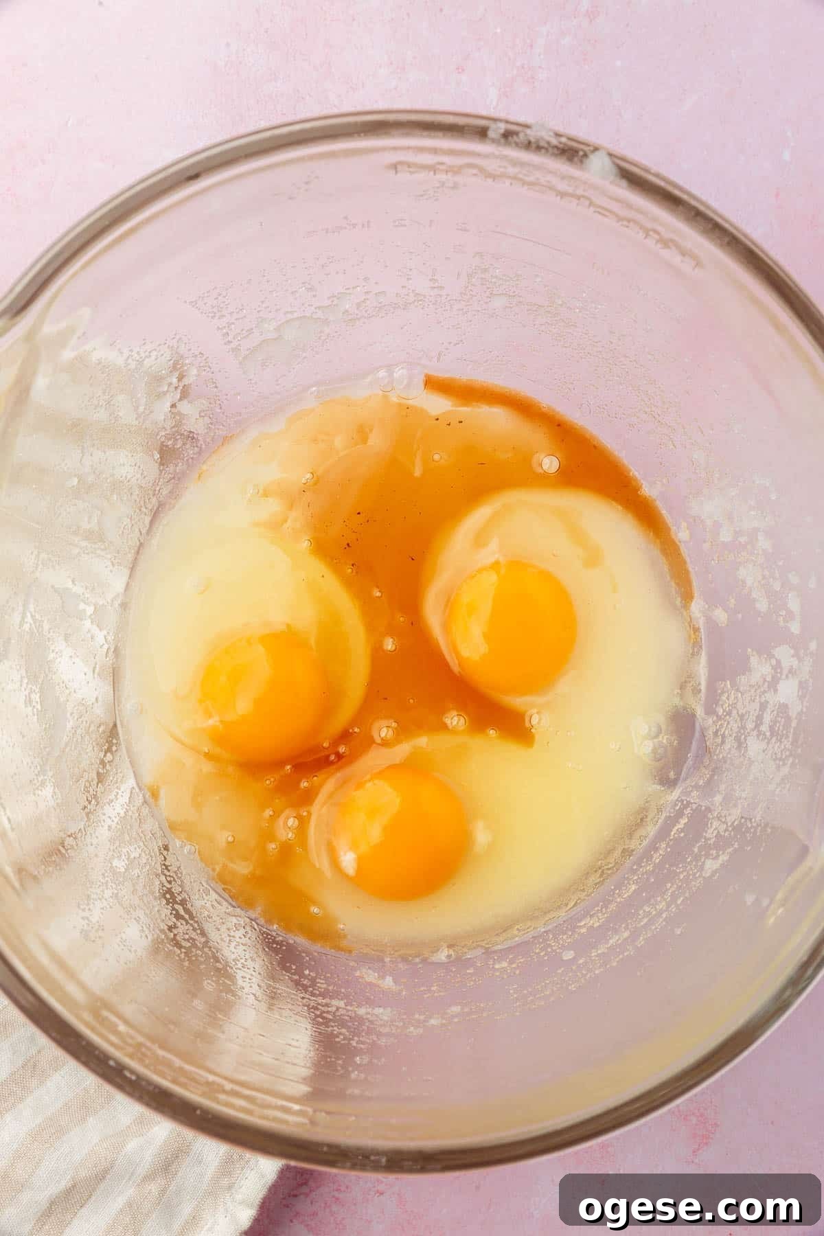 A glass mixing bowl with granulated sugar, oil, vanilla and eggs in it before mixing together.