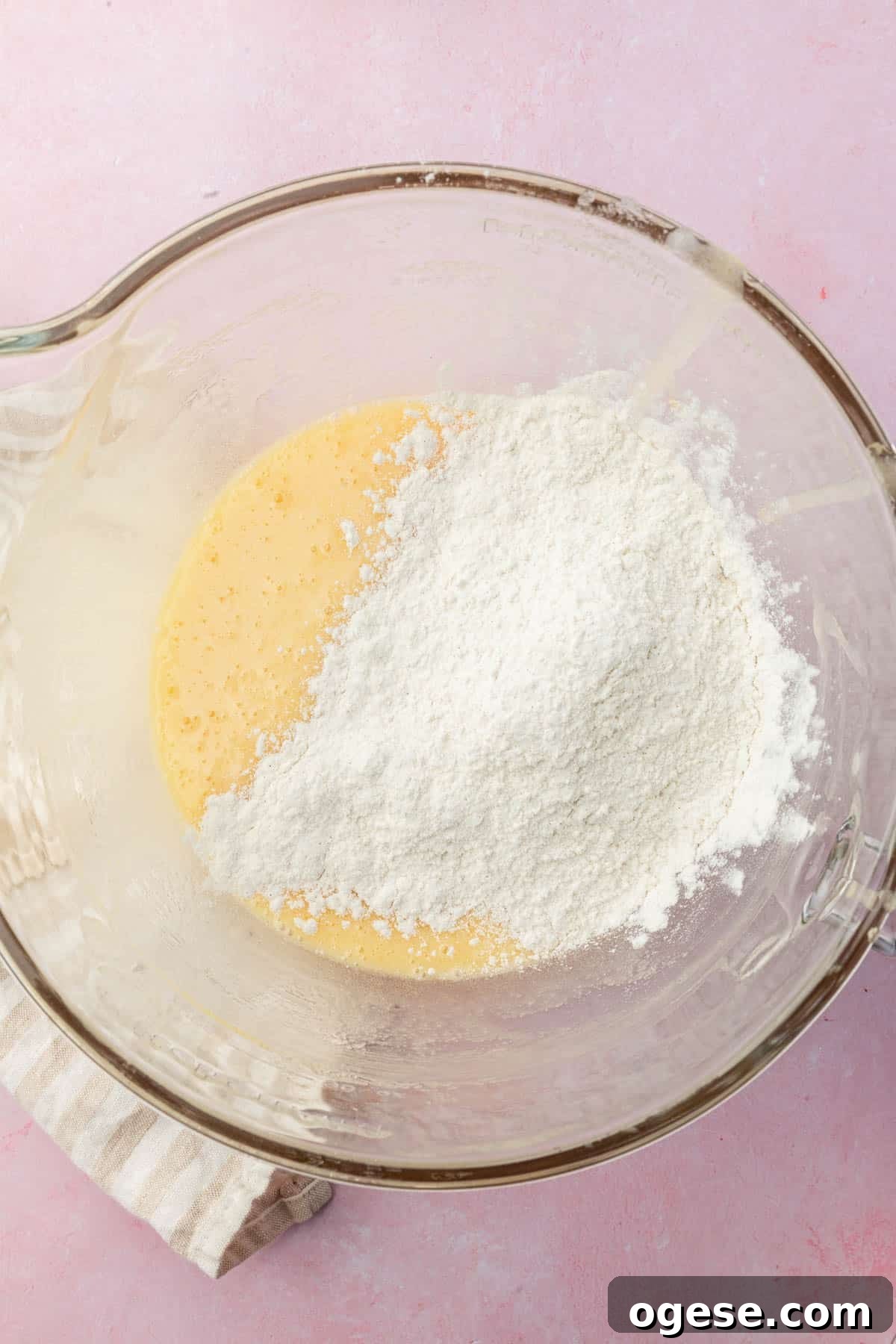 A glass mixing bowl with a cake batter in it topped with a gluten-free flour blend.