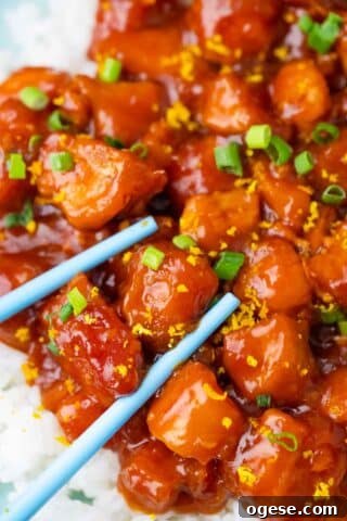 juicy and sticky orange chicken pieces over rice with blue chopsticks next to them