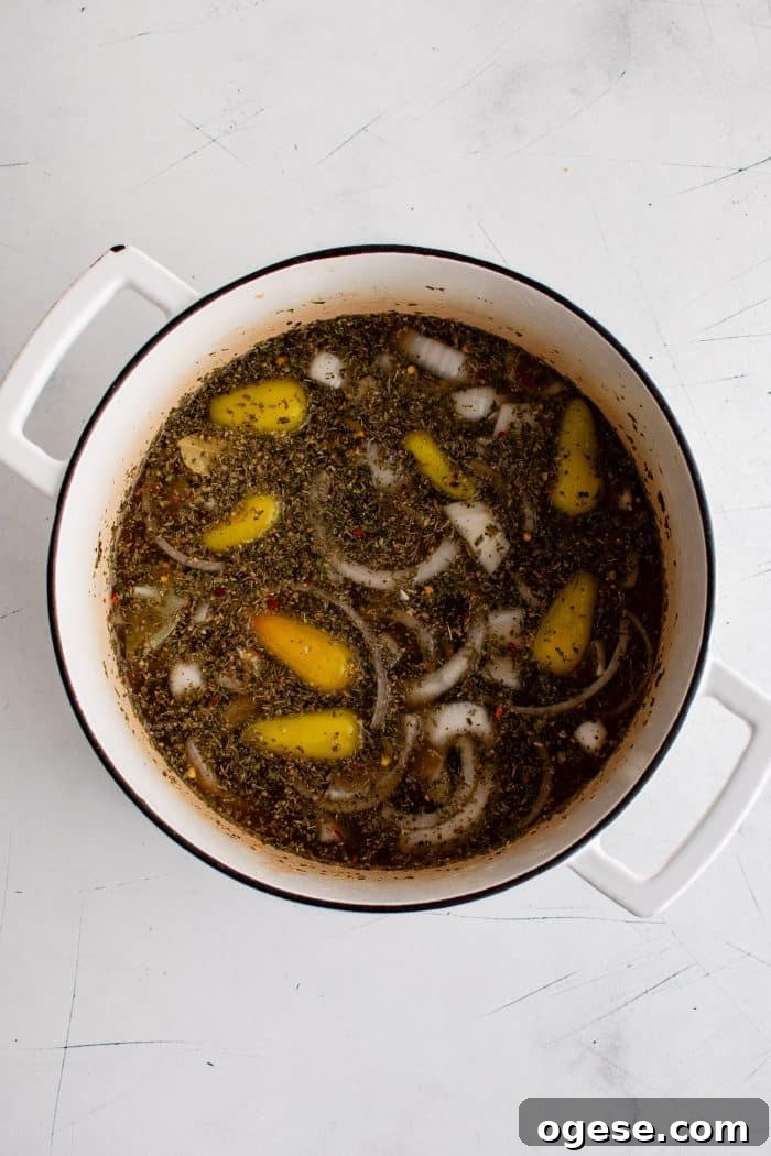 Classic Italian Beef Sandwich Recipe: Tender Slow-Cooked Roast Beef on Italian Bread 8 White Dutch oven filled with beef broth seasoned with whole pepperoncini, sliced onion, whole garlic cloves, and Italian seasonings.