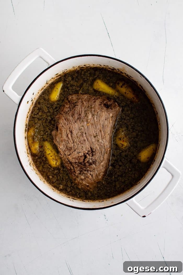 Classic Italian Beef Sandwich Recipe: Tender Slow-Cooked Roast Beef on Italian Bread 9 Large Dutch oven filled with roast beef resting in its own broth seasoned with whole pepperoncinis, sliced onion, and dried Italian seasoning.
