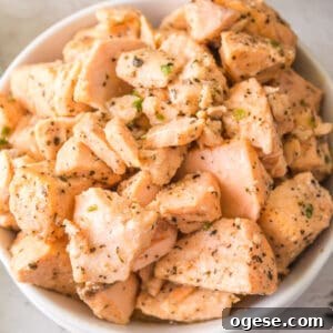 Close-up of a white bowl filled with tender, seasoned air fryer salmon bites coated in garlic butter and herbs.