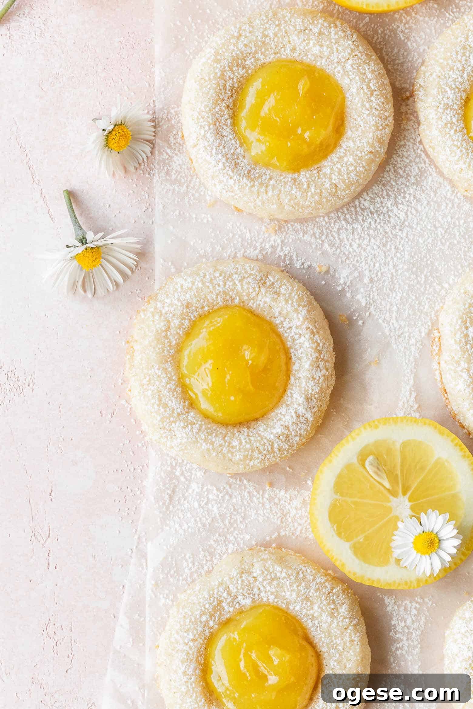 Lemon curd cookies on a pink surface with small white flowers scattered around.