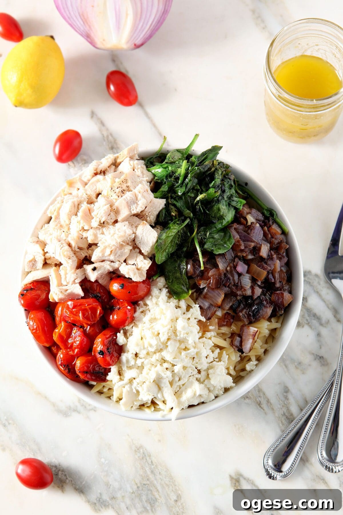 A bowl of ingredients, including charred tomatoes, chicken, wilted spinach, red onion and feta cheese in a bowl on marble