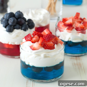 Patriotic 4th of July Fruit and Jello Cups Recipe 6 Three glass cups with festive 4th of July Jello cups: blue gelatin layered with blueberries and whipped cream, one topped with extra blueberries, while the others have strawberries on whipped cream over red or blue gelatin.