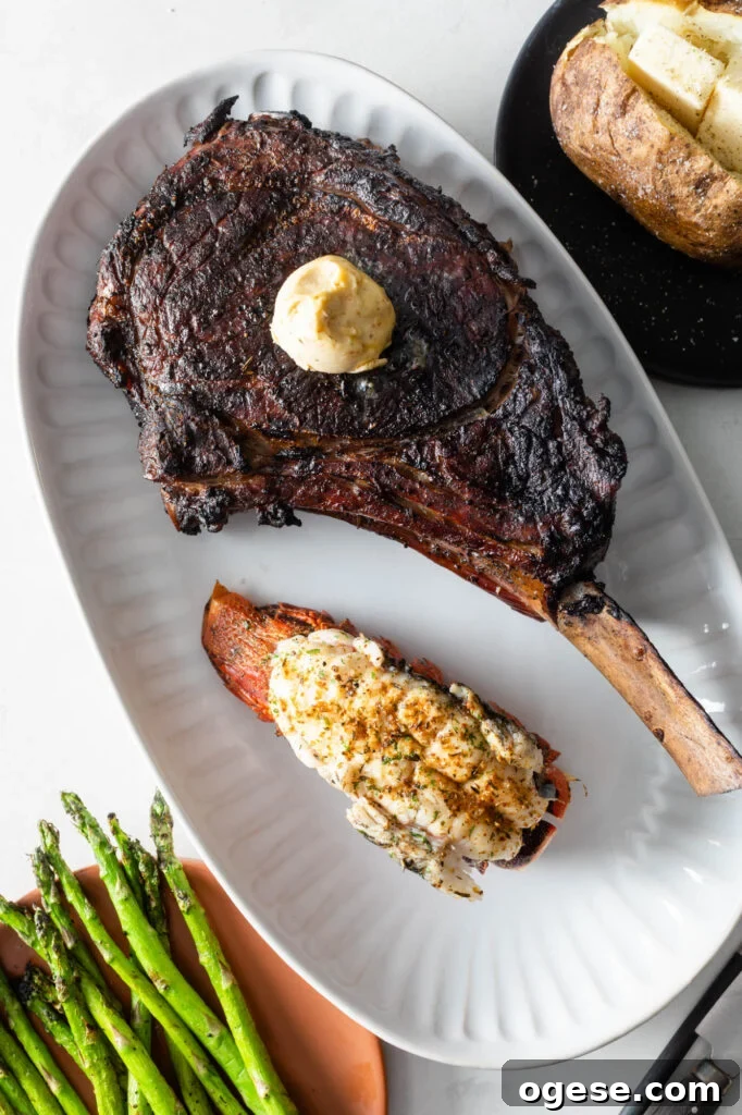 How to Cook a Tomahawk Steak Perfectly Every Time 2 cooked tomahawk steak topped with a scoop of compound butter on a plate with a cooked lobster tail. asparagus spears and a baked potato with butter in the background