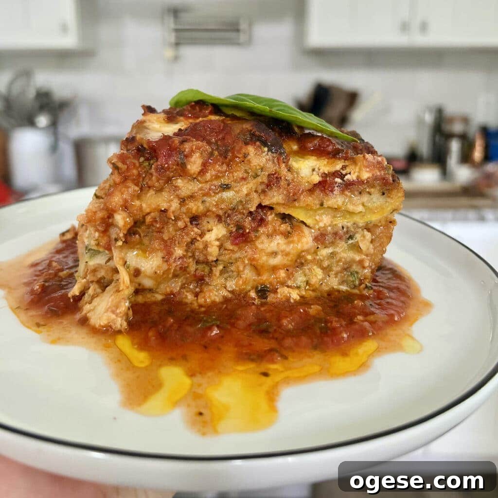 Slice of zucchini parmigiana on white plate with stove and kitchen in background.