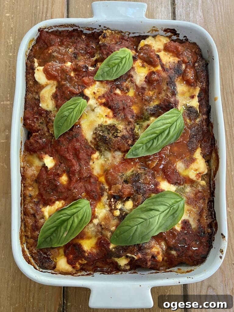 The finished baked zucchini parmigiana (parmesan) in baking dish with basil garnish.