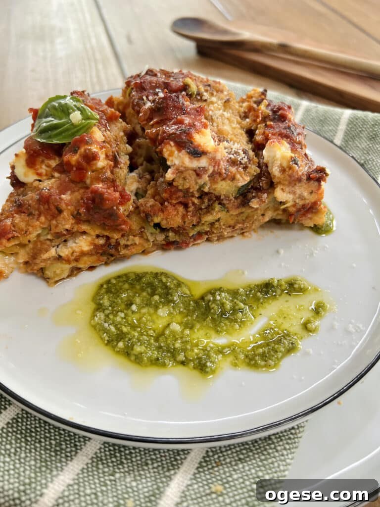 Big piece of zucchini parmesan on plate with pesto garnish and wooden spoon in background.