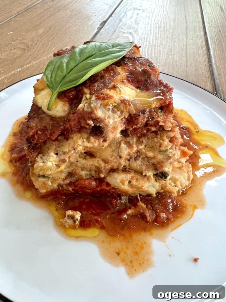 Slice of zucchini parmesan (parmigiana) on white plate with extra sauce.