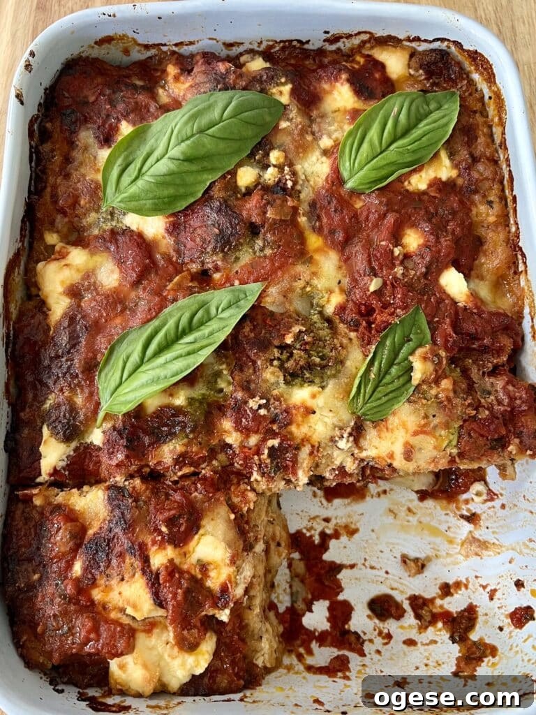 The finished baked zucchini parmigiana (parmesan) in baking dish with basil garnish and one slice cut out.