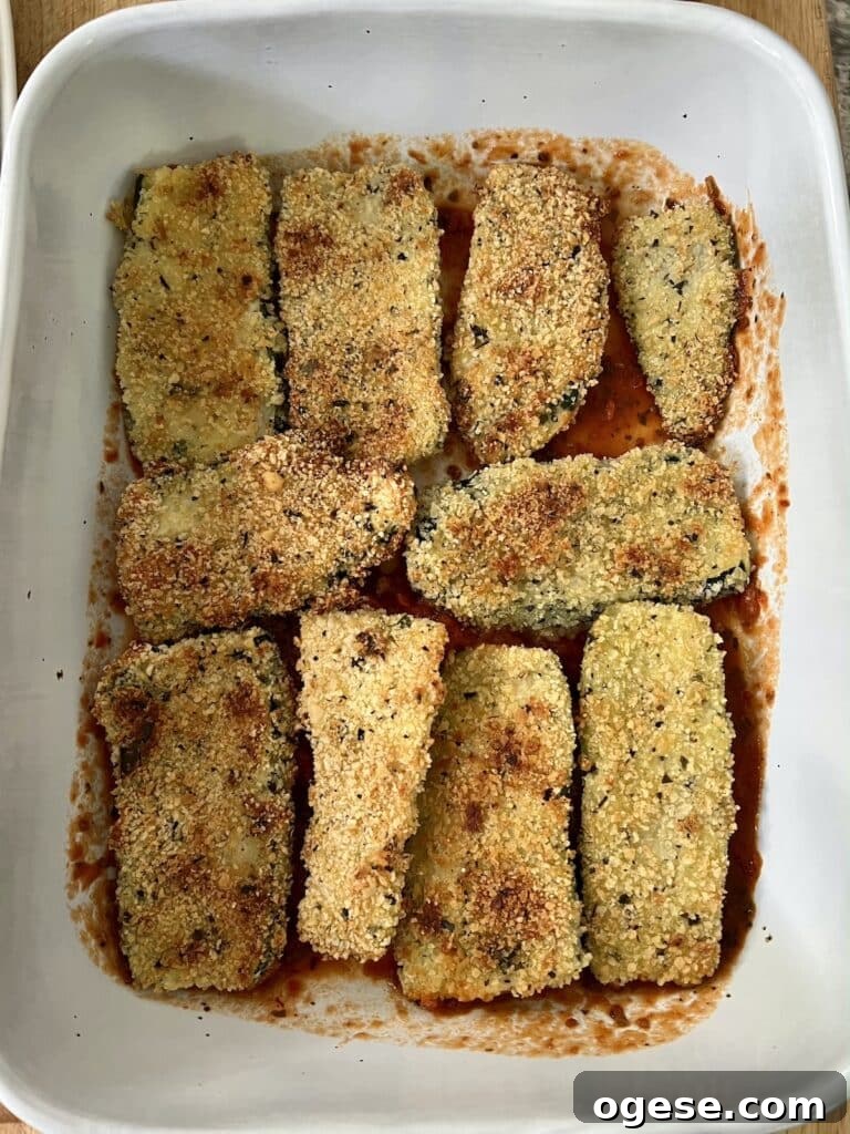 Building the dish: baked, breaded zucchini arranged in single layer over sauce.