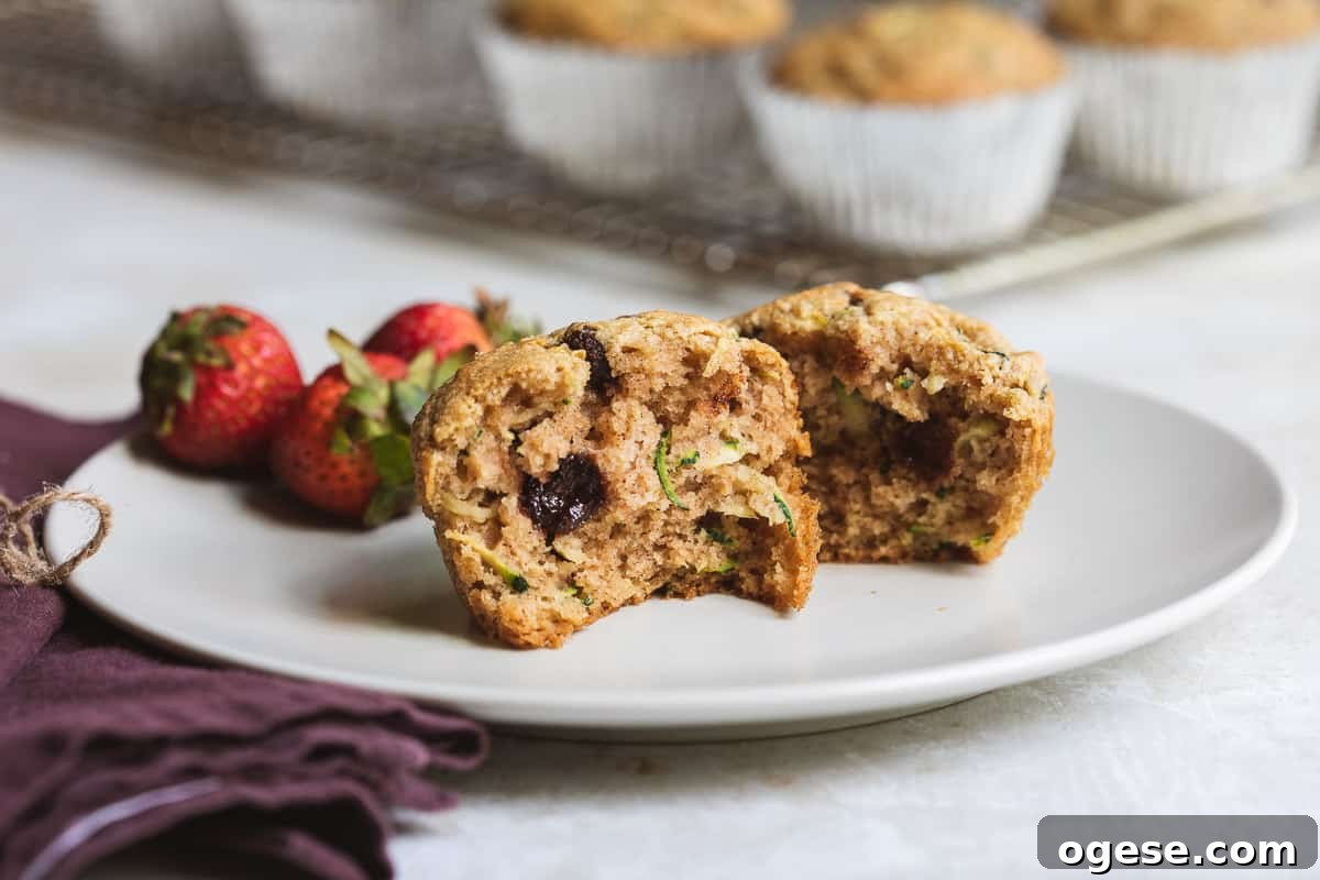 one almond flour zucchini muffin ripped in half on a plate next to strawberries in front of cooling rack.