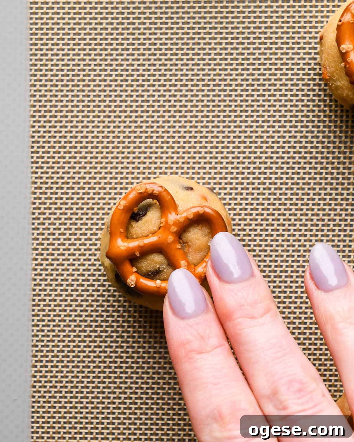 Salted Pretzel Chocolate Chip Cookies: Sweet Meets Crunch 19 a hand pressing a pretzel into the top of a cookie dough ball