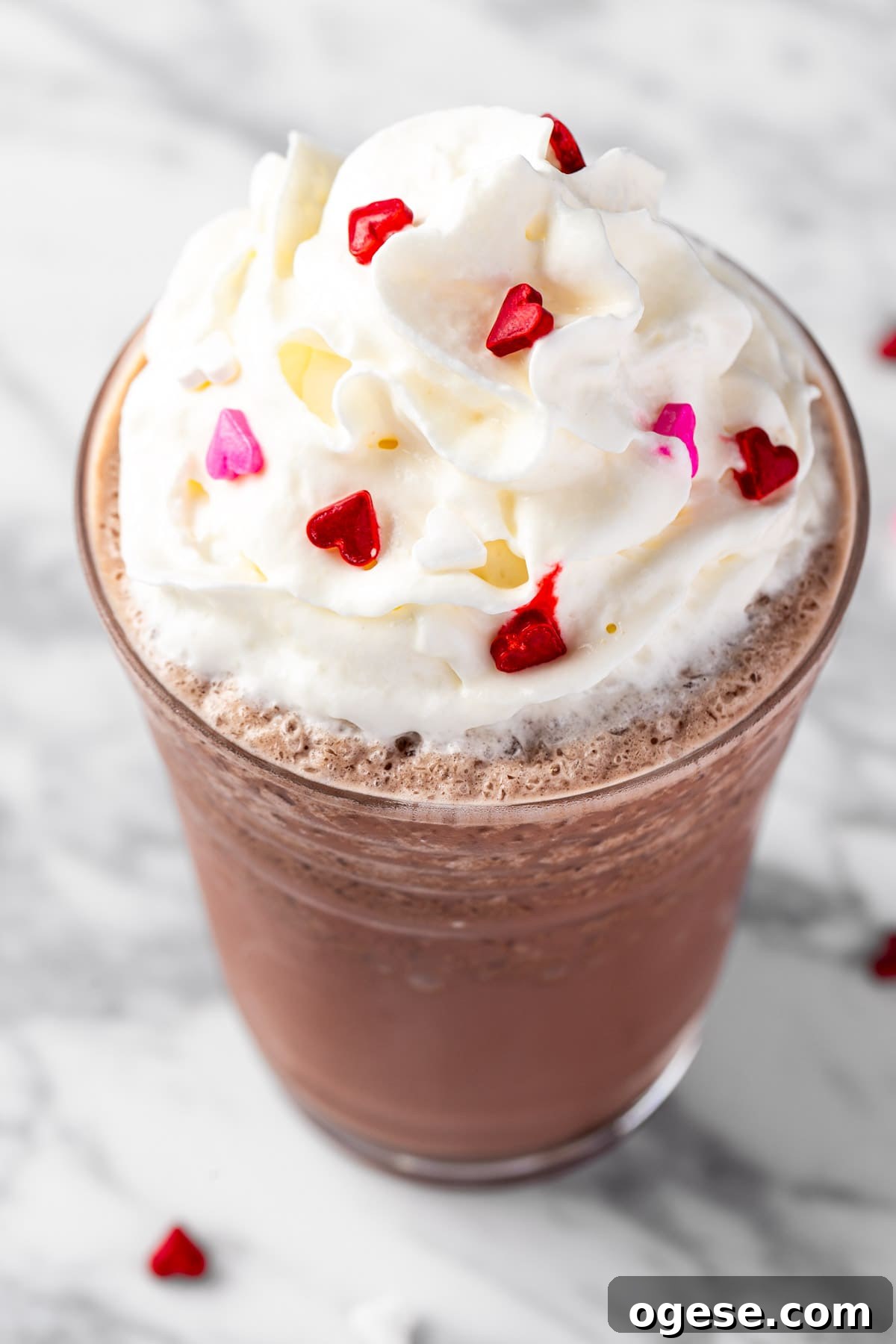 Red Velvet Frappuccino Recipe: Creamy Iced Dessert Drink 2 A red velvet frappuccino topped with whipped cream and heart sprinkles.