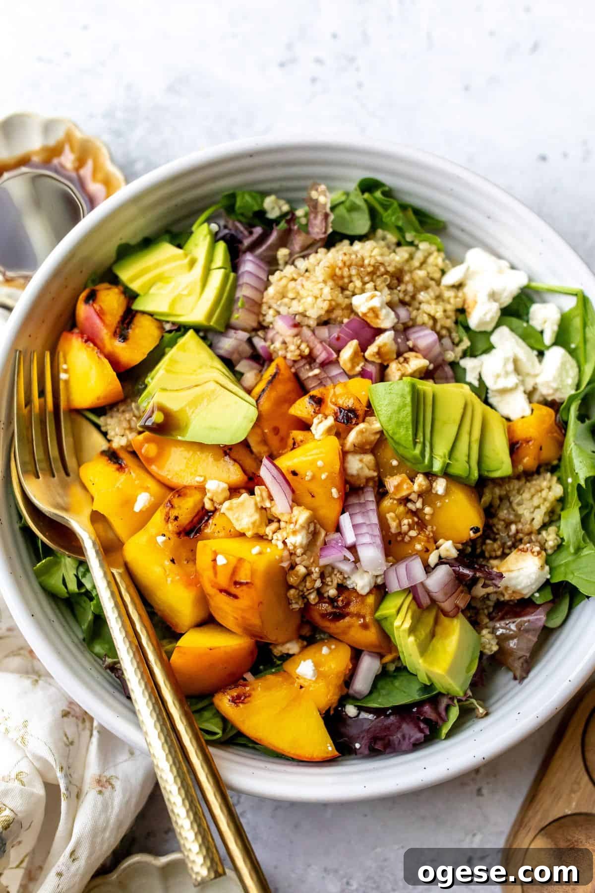 White bowl with peach feta salad and avocado on it, serving utensils to the side.