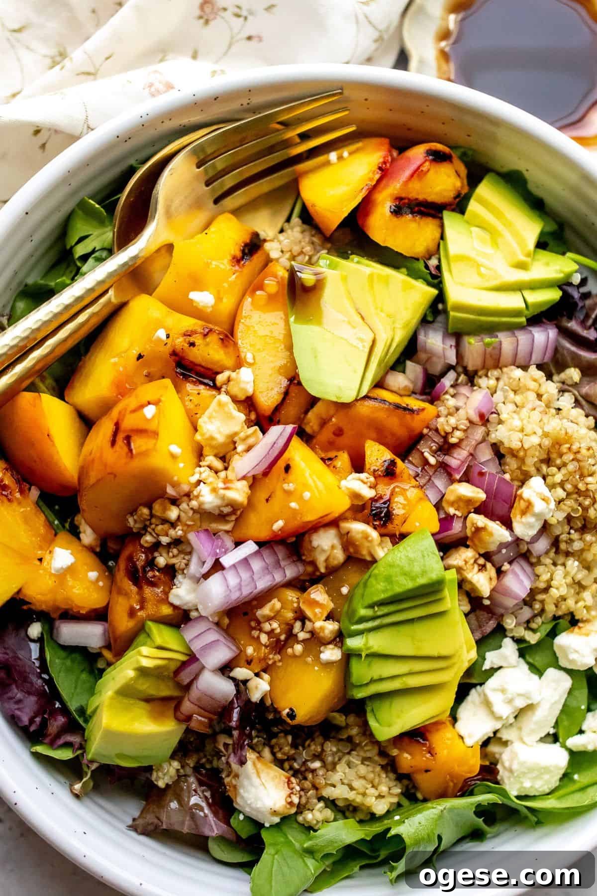White bowl with peach feta salad and avocado on it, serving utensils to the side.