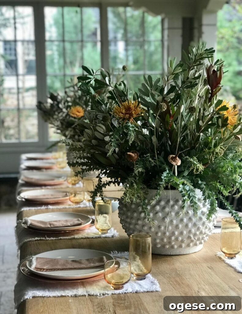 Stylish Thanksgiving Table Decor Ideas for 2021 2 a wooden table with a large white vase of flowers set with yellow glasses, white plates and rust colored napkins