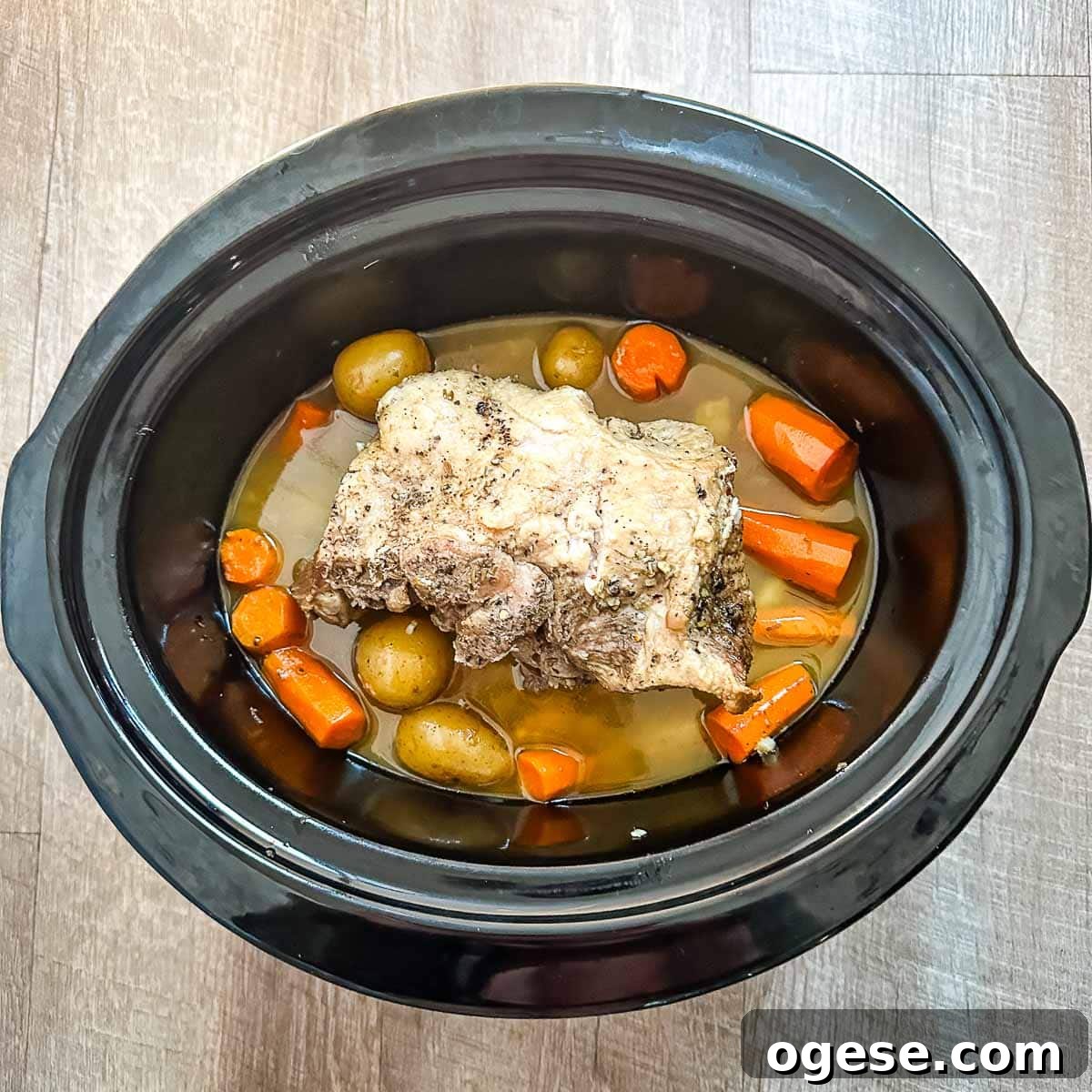 Slow Cooker Italian Pork Roast with Garlic and Herbs 16 Image shows Italian slow cooker pork roast halfway through cook time in a crock pot with potatoes, carrots, and cooking liquid.