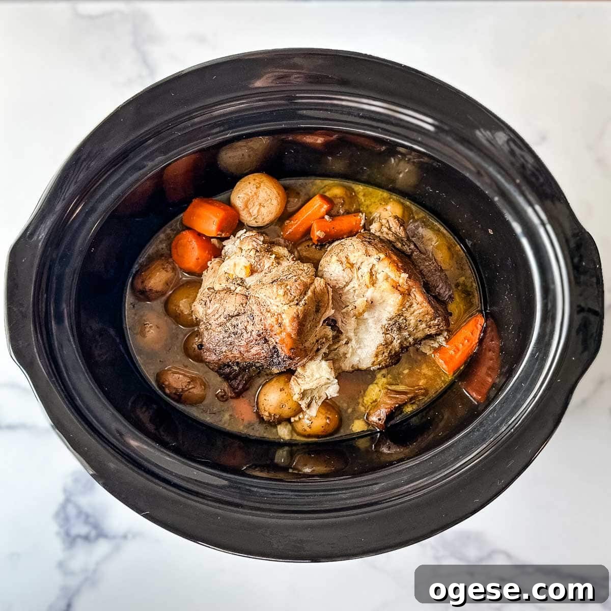 Slow Cooker Italian Pork Roast with Garlic and Herbs 17 A crock pot containing a fully cooked Italian slow cooker pork roast, potatoes, and carrots.
