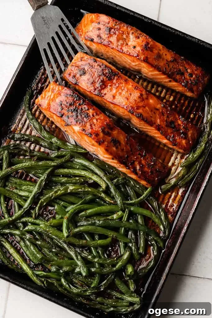 Baked Salmon in Oven oven-baked honey soy salmon and asparagus on a baking sheet with a spatula preparing to scoop one of the filets