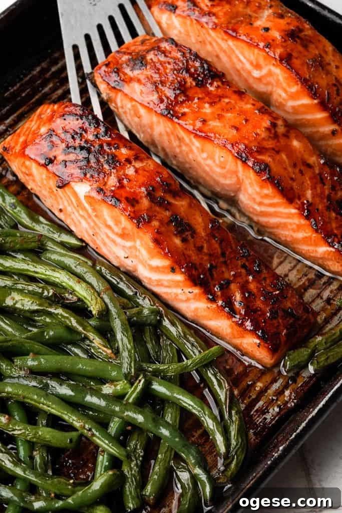 Honey Soy Salmon close up view of honey soy salmon and asparagus on a baking sheet with a spatula preparing to scoop one of the filets