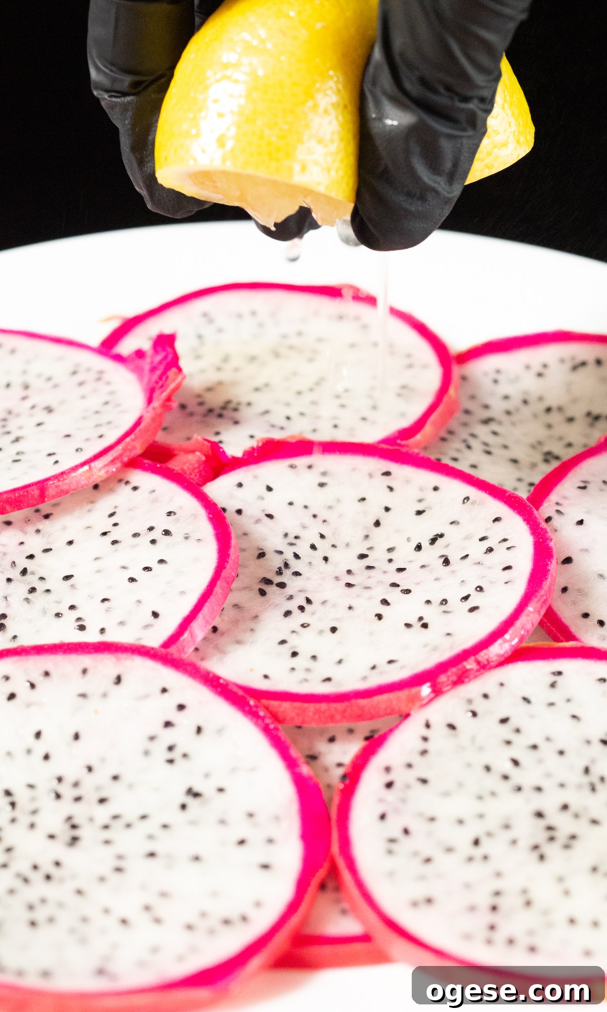 Dehydrated Dragon Fruit Chips: DIY Recipe and Storage Tips 5 Dragonfruit slices in a single layer on a white plate. A hand squeezes fresh lemon juice over the top.