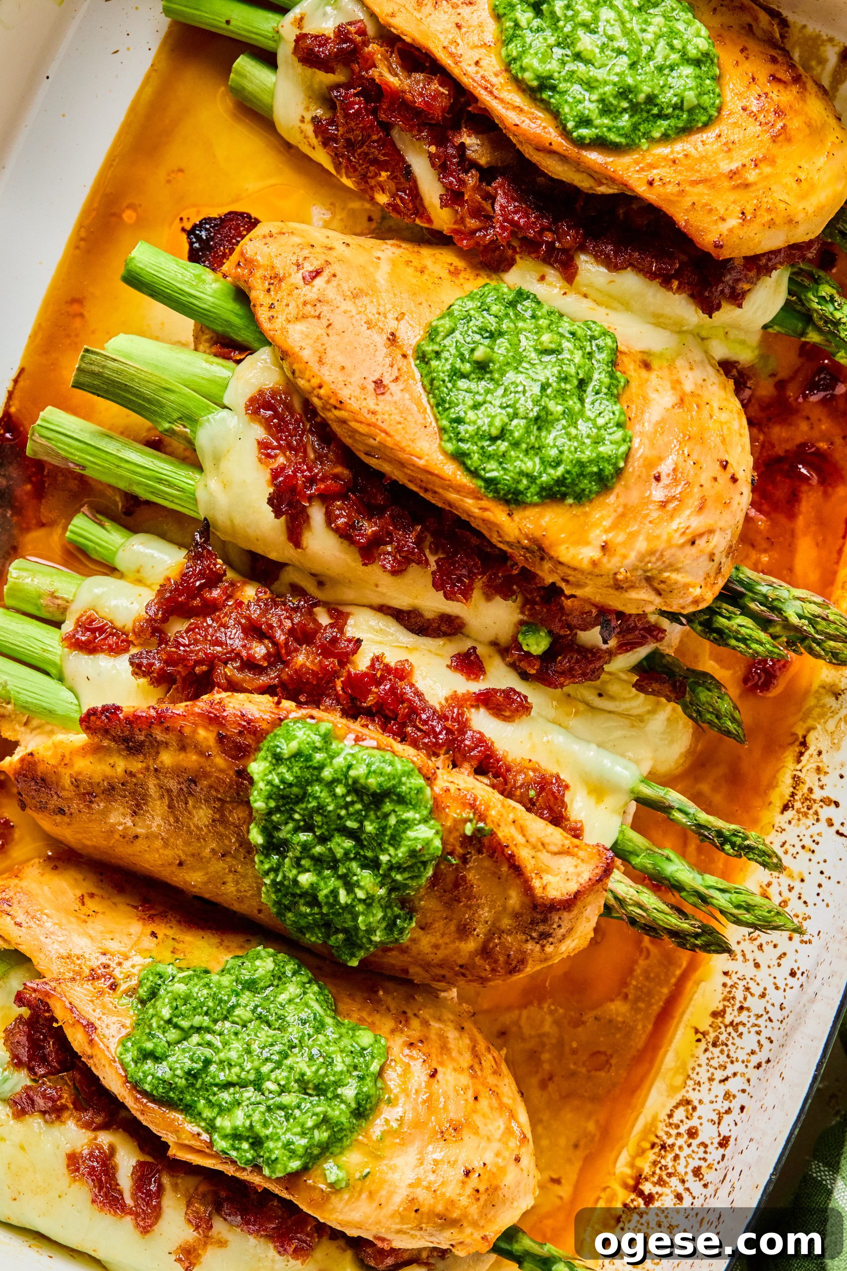 4 asparagus stuffed chicken breasts made with melty mozzarella and sun-dried tomatoes topped with a spoonful or homemade spinach pesto sitting in a large baking dish
