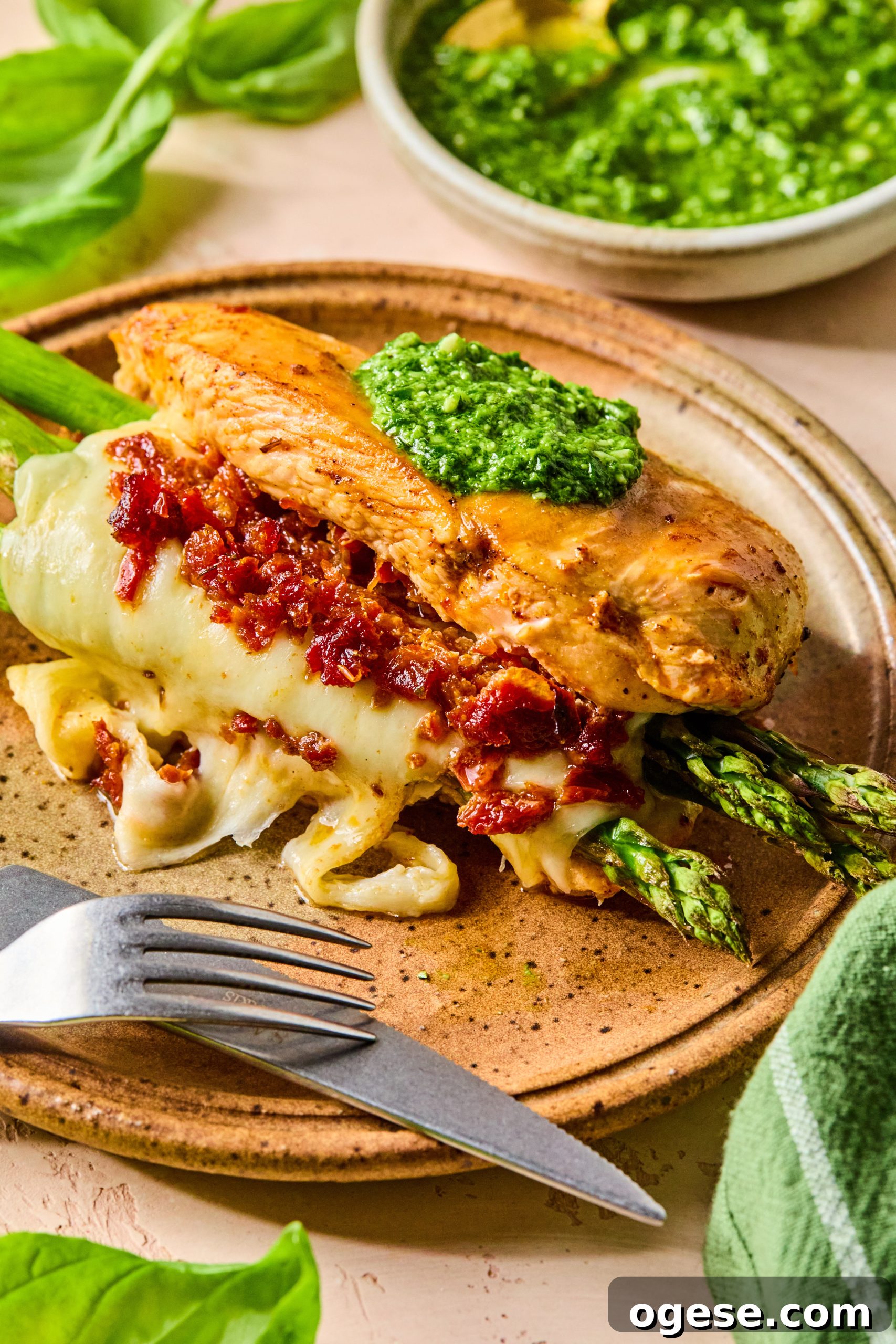 A close up photo of asparagus stuffed chicken made with melty mozzarella cheese, sun-dried tomatoes and a dollop of homemade pesto on top