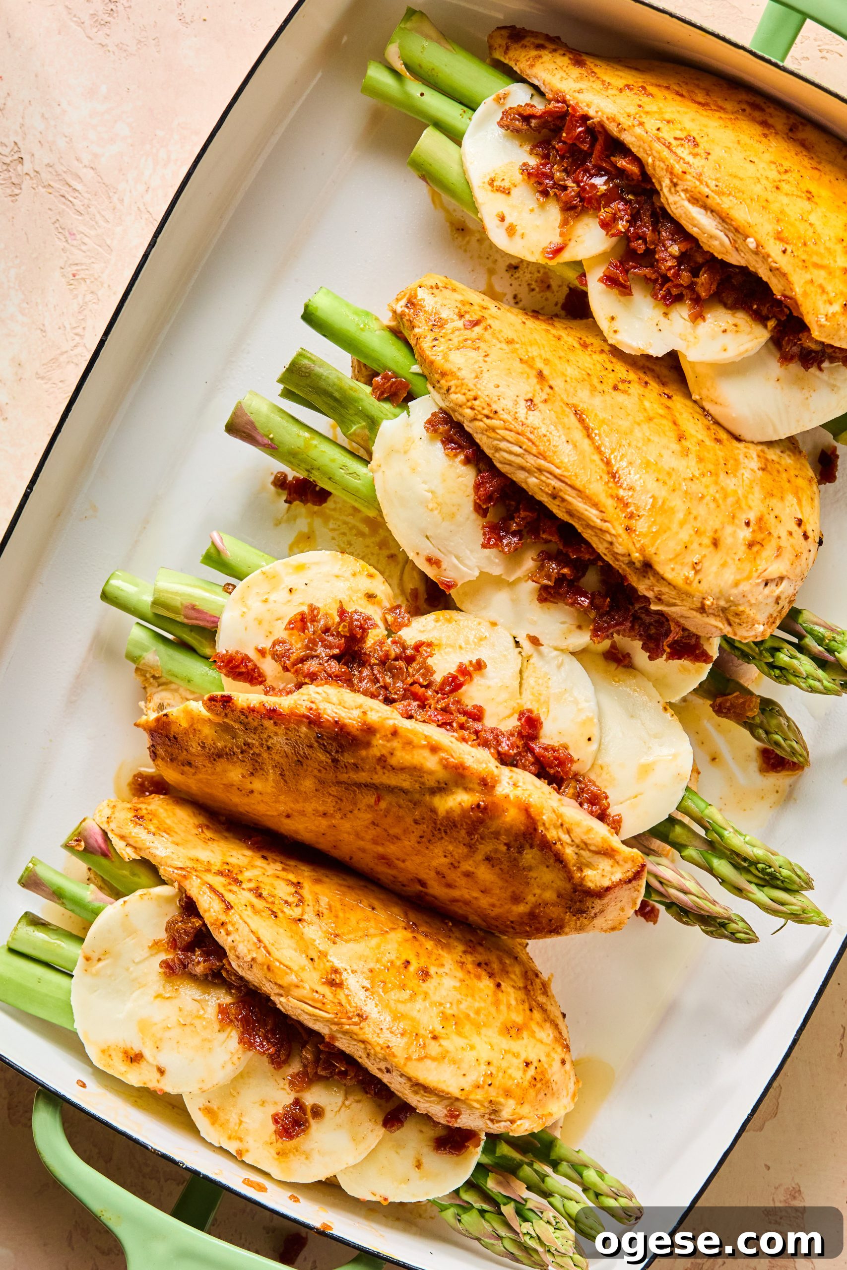 4 seasoned and seared chicken breasts filled with asparagus, sliced mozzarella and sun-dried tomatoes sitting in a large baking dish