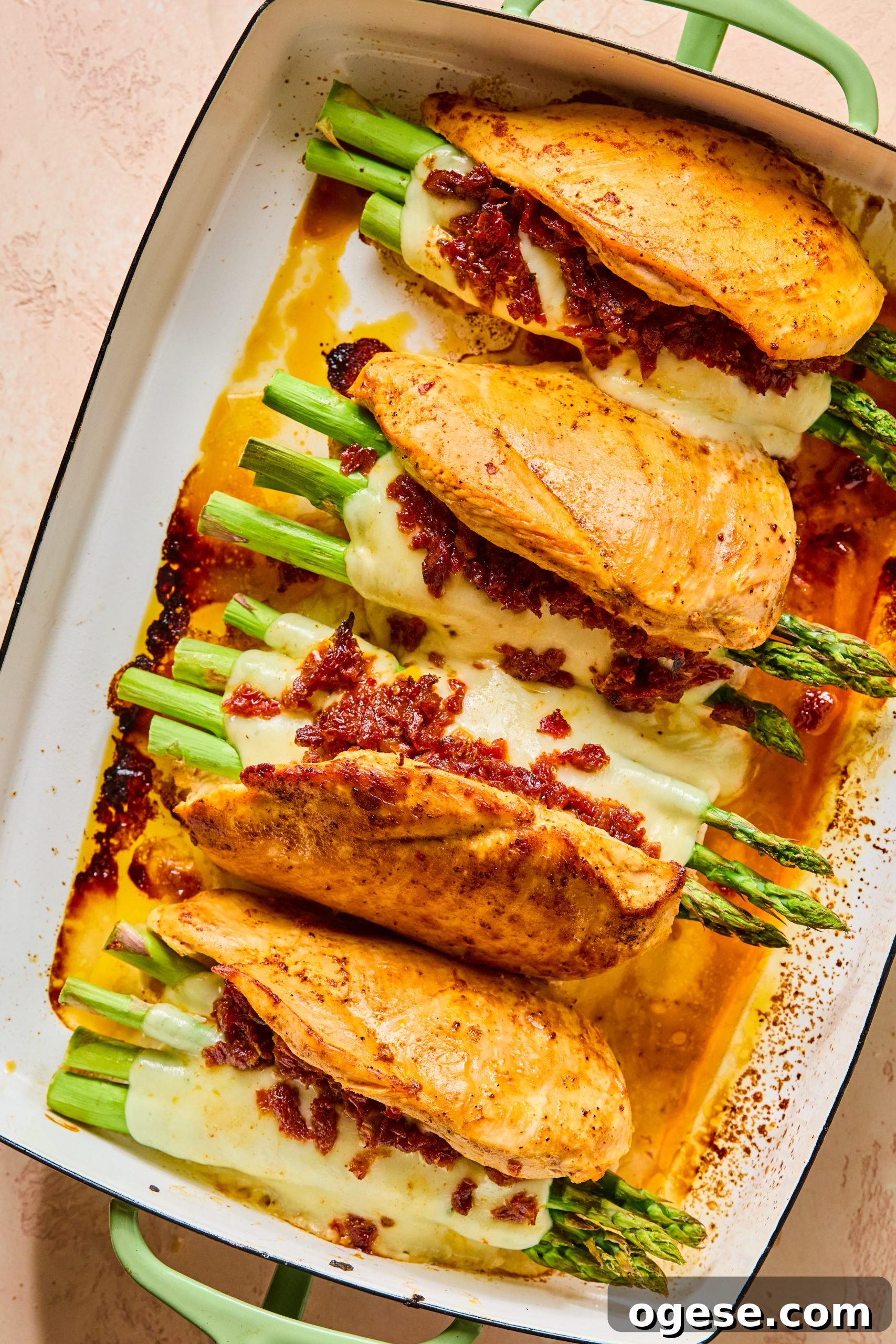 Baked cheesy asparagus stuffed chicken sitting in a hot baking dish with wamr chicken juices and gooey melty mozzarella
