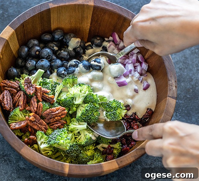 Vegan Broccoli & Blueberry Salad with Lemon Vinaigrette 7 a bowl of vegan broccoli salad being mixed with the dressing using 2 spoons
