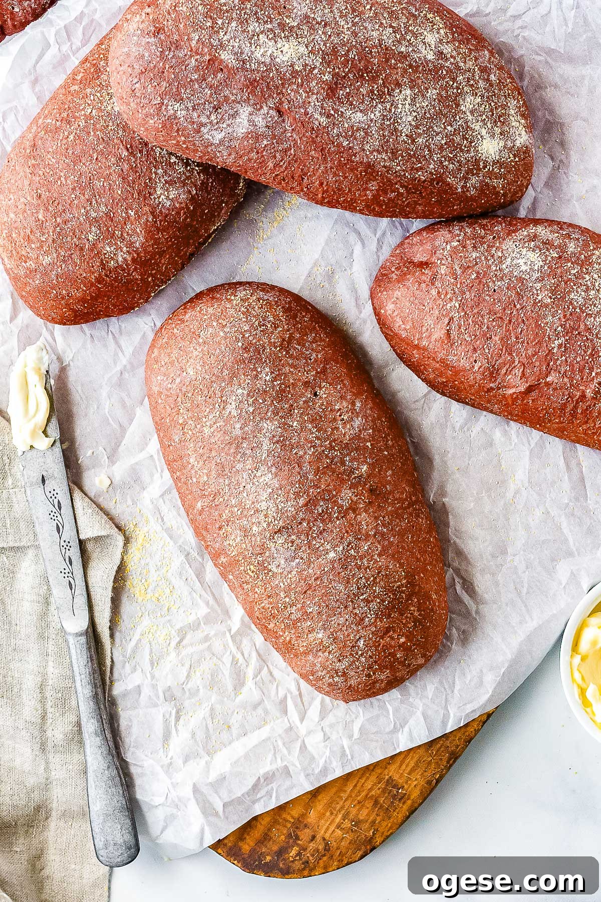Overhead view of freshly baked homemade Outback bread loaves dusted with cornmeal on parchment paper beside butter and a bread knife.