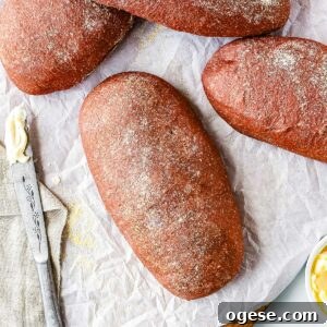 Overhead view of freshly baked homemade Outback bread loaves dusted with cornmeal on parchment paper beside butter and a bread knife.