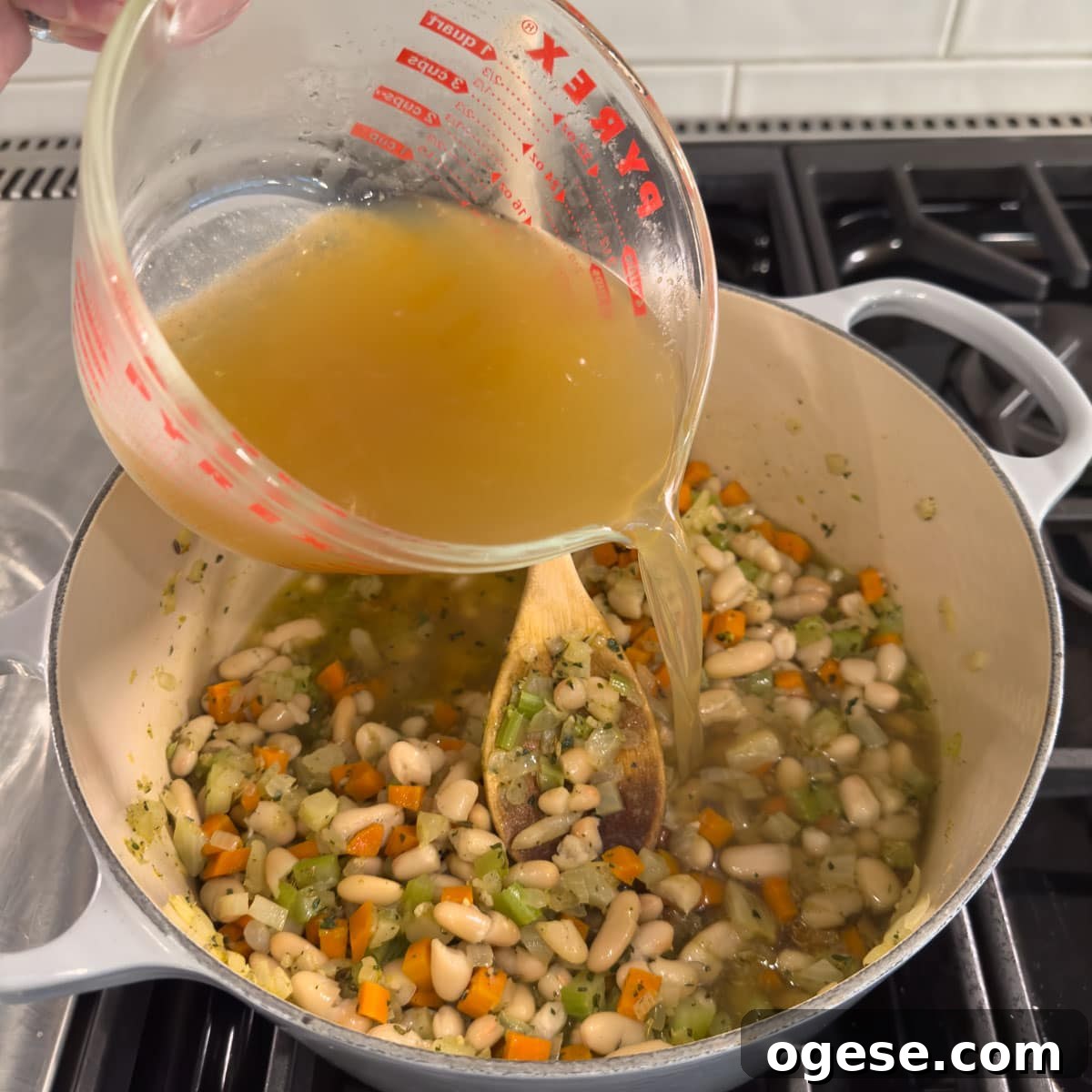 Tuscan White Bean Soup Recipe with Garlic and Kale 6 Pouring golden broth into a pot while making soup.