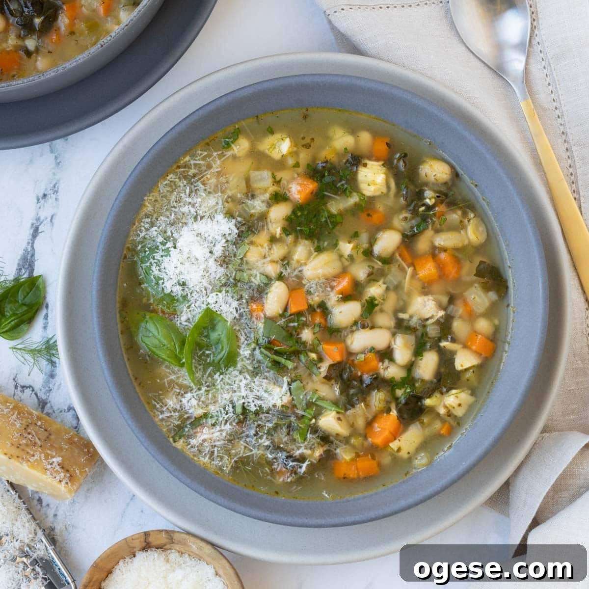 Tuscan White Bean Soup Recipe with Garlic and Kale 10 Gray bowl with bean and kale soup topped with parmesan and basil.